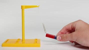 A hand manipulates a magnet near a suspended paperclip, illustrating magnetic forces in a controlled environment with clear lighting video