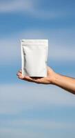 Hand holding a white product bag in front of a blue sky, Mockup of a blank package presented by a person against an airy backdrop photo