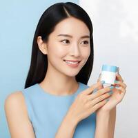Elegant Asian Woman Presenting Skincare Product with Radiant Smile, Beautiful Woman with Clear Skin Holding Moisturizing Cream in Studio Setting photo