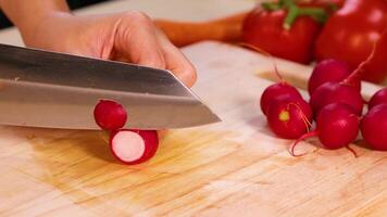 Hands slicing radishes with tomatoes in background video