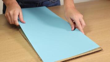Hands methodically fold blue paper on a wooden table under soft lighting, demonstrating a step-by-step process video