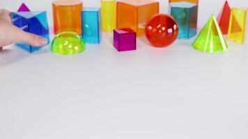 Hands interact with vibrant geometric shapes on a white background, demonstrating movement and arrangement in bright lighting video
