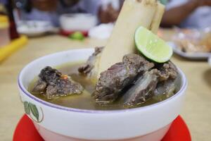 A bowl of soup with meat and a lime wedge photo