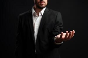 Businessman in formal attire extends hand in welcoming gesture against dark background during networking event photo