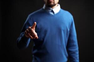 Man in blue sweater gestures confidently with a pointed finger against a dark background photo