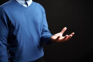 Open-handed gesture of a person wearing a blue sweater against a dark background photo