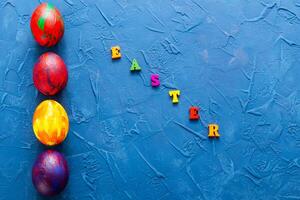 Multicolored wooden letters making up the words happy easter and decorative colourful eggs on a blue background. Top view. photo