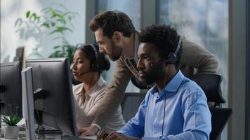 Callcenter teamwork multicultural office operators support communication African man Indian woman headset computer helpdesk Caucasian supervisor pointing monitor giving instructions customer service photo