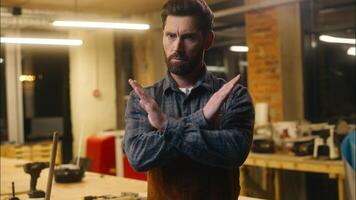 Serious Caucasian wood master man show prohibition gesture in workshop craftsman forbid builder joiner rejection guy demonstrating cross with hands male repairman ban no symbol artist decline refusing photo