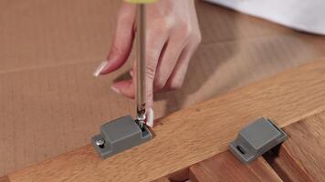 Close-up of hands using a screwdriver to assemble furniture on a wooden surface in a well-lit environment video