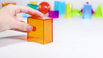 A hand interacts with vibrant 3D geometric shapes on a white surface, highlighting educational and playful elements video