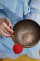 Female hand holding wooden mallet above metal singing bowl. Image suitable for meditation, mindfulness, or sound therapy context. photo