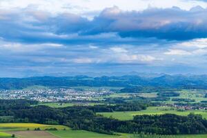 View of a forest, fields and village on the hills against a cloudy sky photo