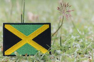 Jamaica flag Eco friendly JAM flag crafted from colorful threads, lying on natural grass with wildflowers. Horizontal image with copy space for text. Earth day, calm nature vibe. photo