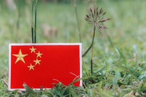 Eco friendly Chinese flag embroidered from colorful threads lying on grass with small flowers. Horizontal photo with copy space on the right. Earth day, climate change.