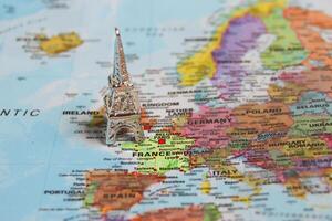 Studio photo of a miniature silver Eiffel Tower positioned over France on a colorful world map, symbolizing travel plans, Paris dreams, and European journeys.