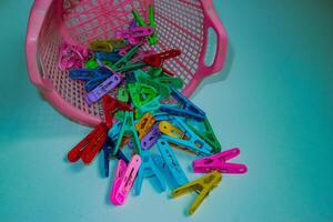 Playful design Colorful plastic clothespins scattered from pink basket on blue-green background. Playful everyday household objects in bright, abstract pop art flat lay. photo