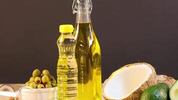 A variety of oils and foods including avocados, coconuts, and almonds arranged on a table with warm lighting video