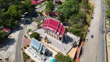 Drone footage captures the vibrant red-roofed Wat Nai Harn Temple in Phuket, Thailand, surrounded by lush greenery and clear skies video