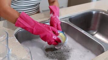 A person cleans a colander in a kitchen sink using pink gloves and a sponge video