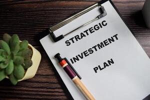 Concept of Strategic investment plan write on clipboard isolated on Wooden Table. photo