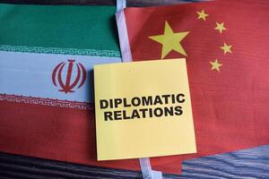 Concept of Diplomatic relations write on sticky notes with iran flag and china flag isolated on Wooden Table. photo