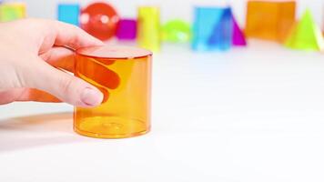 A hand interacts with vibrant 3D geometric shapes on a white surface, illustrating basic mathematical concepts in a playful setting video