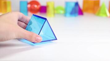 A hand interacts with colorful 3D geometric shapes on a white surface, demonstrating movement and balance video
