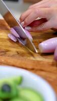 Close-up of hands slicing shallots on a wooden board with a knife, under bright kitchen lighting video