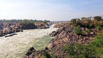 Dynamic view of Khone Phapheng Falls with powerful water flow, rocky terrain, and lush greenery under bright daylight video
