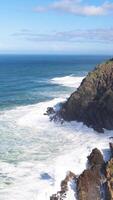 Dynamic ocean waves crash against rugged cliffs under a bright blue sky, capturing the power and beauty of nature video