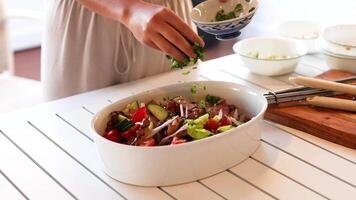 Hands adding coriander to a colorful beef salad in a bright kitchen setting, emphasizing freshness and culinary artistry video