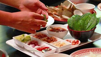 Hands assemble Miang Kham with fresh ingredients on a table in Phuket. Bright lighting highlights the vibrant colors and textures video