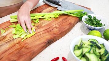 Hands skillfully chop celery on a wooden board, surrounded by fresh ingredients in a well-lit kitchen video