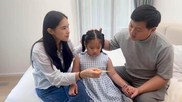 Parents attentively care for their young daughter, checking her temperature in a softly lit bedroom setting video