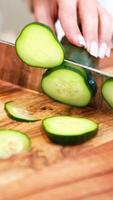 Close-up of hands slicing cucumber on a wooden board. Bright lighting highlights fresh produce and precise knife skills video