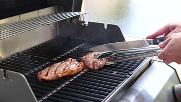 A person grills a beef steak on a barbecue, using tongs to flip it. Bright lighting enhances the cooking process video