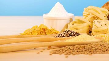 A variety of grains, pasta, and bread arranged on a wooden surface with a blue background, under bright lighting video