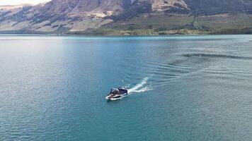 A speedboat glides across Glenorchy's tranquil lake, surrounded by majestic mountains under clear skies video