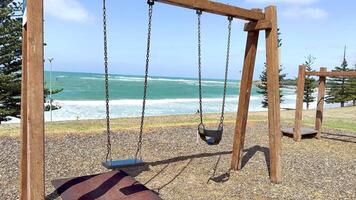 Wooden swings stand still by the ocean in Torquay, Australia. Bright daylight highlights the serene coastal setting video