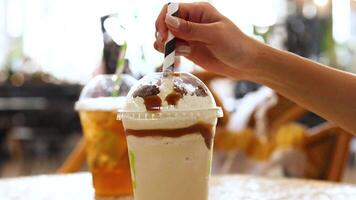 A hand stirs a creamy drink topped with caramel, set against a bright cafe background in Gold Coast, Australia video