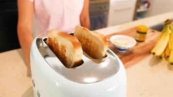 Slices of bread pop from a toaster on a kitchen counter with bananas and a jar nearby video