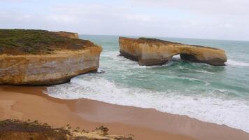 Aerial view of waves hitting the London Bridge rock formation at Port Campbell, Australia. Overcast lighting highlights the rugged coastline video