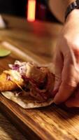 Hands assemble a fish taco with toppings on a wooden board under warm lighting video