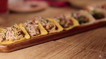 A series of tacos arranged on a wooden platter in a warmly lit restaurant setting, highlighting vibrant ingredients video