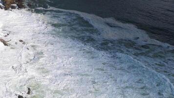 Aerial view of powerful ocean waves crashing against rocky shoreline at Byron Bay, captured in natural daylight video