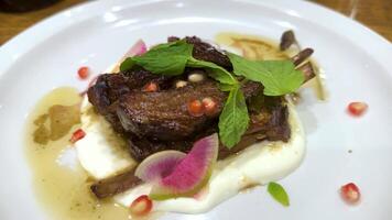 A beautifully plated rib steak with fresh greens, pomegranate seeds, and vibrant garnishes on a white plate video