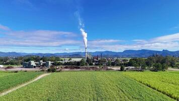 Drone footage captures a rural landscape with fields and a factory emitting smoke under clear blue skies video