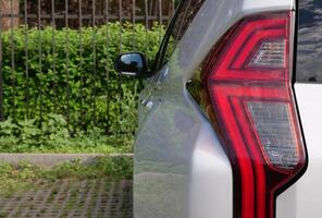 Rear LED Lights Of Large SUV With Fence And Green Hedge On Background photo