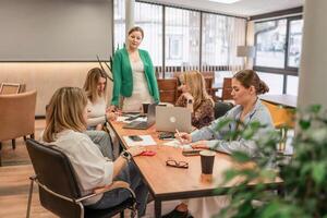 Businesswomen Meeting Laptops. Team brainstorms at office table, daytime, for project development discussion. photo